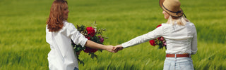 Two women holding hands with flowers in a green field
